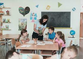 Female Teacher with kids in biology class at elementary school conducting biology or botanical scientific experiment about sustainable Growing plants. Learning about plants in a glass jar photo