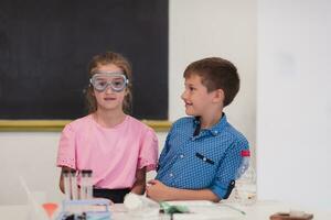 Elementary School Science Classroom Enthusiastic Teacher Explains Chemistry to Diverse Group of Children, Little Boy Mixes Chemicals in Beakers. Children Learn with Interest photo