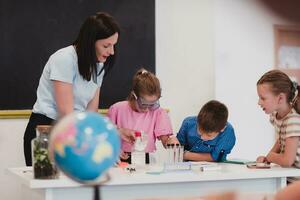 Elementary School Science Classroom Enthusiastic Teacher Explains Chemistry to Diverse Group of Children, Little Boy Mixes Chemicals in Beakers. Children Learn with Interest photo