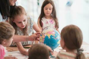 Female teacher with kids in geography class looking at globe. Side view of group of diverse happy school kids with globe in classroom at school. photo