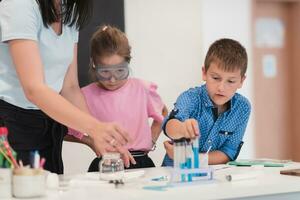 Elementary School Science Classroom Enthusiastic Teacher Explains Chemistry to Diverse Group of Children, Little Boy Mixes Chemicals in Beakers. Children Learn with Interest photo