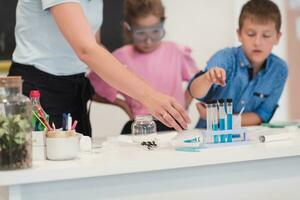 Elementary School Science Classroom Enthusiastic Teacher Explains Chemistry to Diverse Group of Children, Little Boy Mixes Chemicals in Beakers. Children Learn with Interest photo