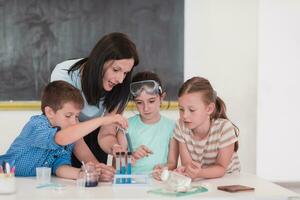 Elementary School Science Classroom Enthusiastic Teacher Explains Chemistry to Diverse Group of Children, Little Boy Mixes Chemicals in Beakers. Children Learn with Interest photo