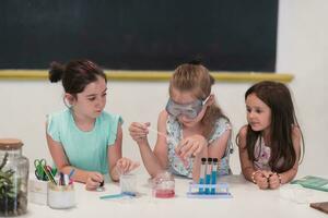 Elementary School Science Classroom Enthusiastic Teacher Explains Chemistry to Diverse Group of Children, Little Boy Mixes Chemicals in Beakers. Children Learn with Interest photo