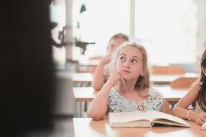 Little girls sitting in elementary school drawing on paper with their friends while sitting in a modern classroom photo