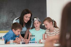 Elementary School Science Classroom Enthusiastic Teacher Explains Chemistry to Diverse Group of Children, Little Boy Mixes Chemicals in Beakers. Children Learn with Interest photo