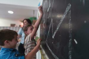 niños escribir y dibujar en el pizarra en elemental colegio mientras aprendizaje el lo esencial de educación foto