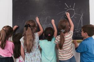 niños escribir y dibujar en el pizarra en elemental colegio mientras aprendizaje el lo esencial de educación foto