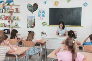 A teacher reads a book to elementary school students who listen carefully while sitting in a modern classroom photo