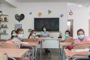 multirracial grupo de niños vistiendo cara mascaras trabajando a clase, escritura y escuchando explicaciones de profesor en salón de clases foto