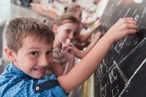 niños escribir y dibujar en el pizarra en elemental colegio mientras aprendizaje el lo esencial de educación foto