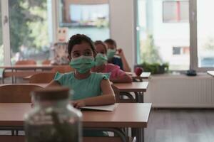 multirracial grupo de niños vistiendo cara mascaras trabajando a clase, escritura y escuchando explicaciones de profesor en salón de clases foto