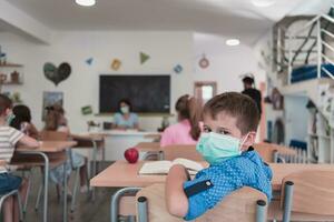 multirracial grupo de niños vistiendo cara mascaras trabajando a clase, escritura y escuchando explicaciones de profesor en salón de clases foto