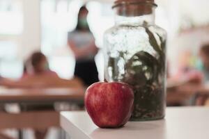 Biology and biochemistry classes. A close-up photo of a bottle containing a green plant and a ripe apple next to the bottle