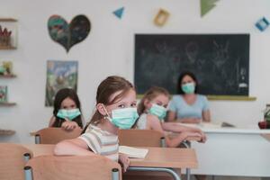 multirracial grupo de niños vistiendo cara mascaras trabajando a clase, escritura y escuchando explicaciones de profesor en salón de clases foto