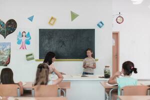 Elementary school. The female teacher helping the child student while writing the answer on the chalkboard. photo