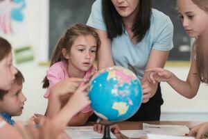 Female teacher with kids in geography class looking at globe. Side view of group of diverse happy school kids with globe in classroom at school. photo