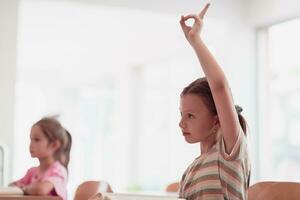 el niña levanta su mano mientras participativo en un proyecto en un moderno preescolar institución. selectivo atención foto