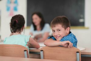 Little boy sitting in elementary school drawing on paper with their friends while sitting in a modern classroom photo