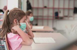 Multiracial group of kids wearing face masks working at class, writing and listening explanations of teacher in classroom photo