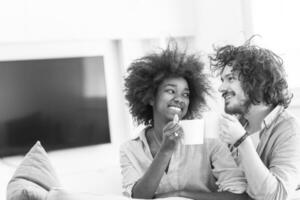 pareja multiétnica sentada en un sofá en casa bebiendo café foto