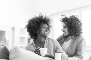 multiethnic couple sitting on sofa at home drinking coffe photo