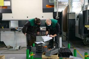 two workers wearing a protective mask due to a coronavirus pandemic, working in a modern factory and preparing a program and materials for a cnc machine photo