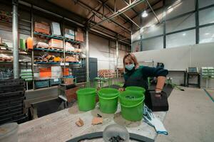 a woman working in a metal factory wears a mask on her face due to a coronavirus pandemic and prepares a piece of metal to be processed by a cnc machine photo