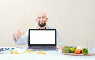 Smiling nutritionist pointing at an advertisement on the laptop, Nutritionist man pointing at laptop screen. Professional nutritionist pointing at blank laptop screen photo