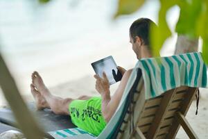 hombre relajándose y usando tableta en la playa foto