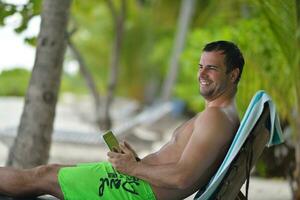 hombre relajándose y usando tableta en la playa foto