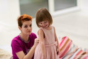 young mother helping daughter while putting on a dress photo