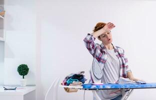 Red haired woman ironing clothes at home photo