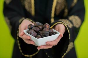 moderno musulmán mujer participación un plato lleno de dulce fechas en iftar hora en Ramadán kareem islámico sano comida concepto OVNI verde antecedentes foto