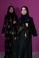 Two beautiful muslim woman in fashinable dress with hijab isolated on modern pink background representing concept of modern islam and ramadan kareem photo