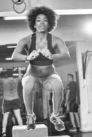 black female athlete is performing box jumps at gym photo