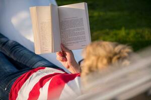 woman reading a book while relaxing on hammock photo