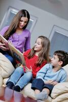 mamá joven juega con sus hijos en casa y lee libros foto