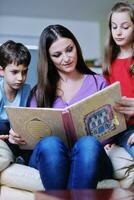 mamá joven juega con sus hijos en casa y lee libros foto