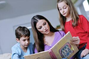 mamá joven juega con sus hijos en casa y lee libros foto