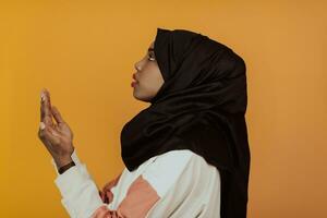 African muslim woman wearing hijab and traditional muslim clothes posing in front of yellow background photo