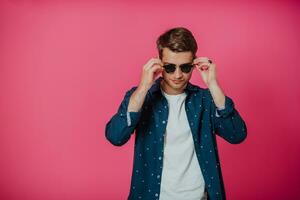 A portrait of a young man wearing a blue shirt and posing in front of a pink background photo