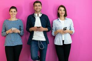 Diverse teenagers using smartphone while posing for a studio photo in front of a pink background