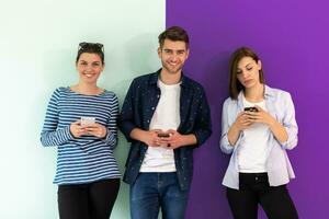 Diverse teenagers using mobile devices while posing for a studio photo in front of a colorful background