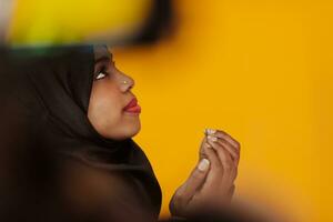 African muslim woman wearing hijab and traditional muslim clothes posing in front of yellow background photo