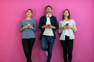 Diverse teenagers using smartphone while posing for a studio photo in front of a pink background