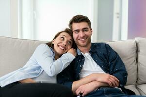 Couple Watches TV together while Sitting on a Couch in the Living Room. Girlfriend and Boyfriend embrace, cuddle, talk, smile and watch Television Streaming Services. Home with Cozy Stylish Interior. photo