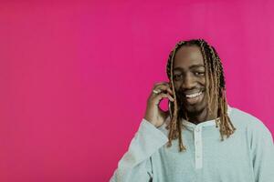 Modern young african student isolated on pink background using smartphone photo