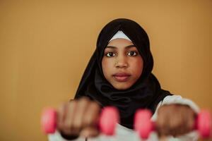 African American muslim woman promotes a healthy life, holding dumbbells in her hands photo
