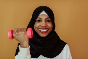 African American muslim woman promotes a healthy life, holding dumbbells in her hands photo